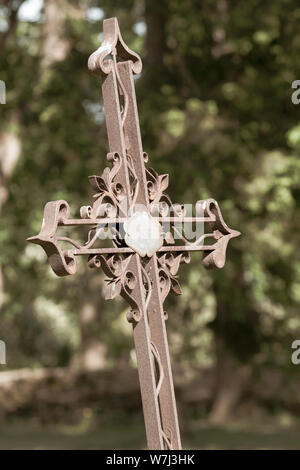 Geneigt alten Curly Eisen geschmiedet Kreuz. Grüner Hintergrund mit unscharfen Laub. Selektiver Fokus auf das Kreuz. Stockfoto