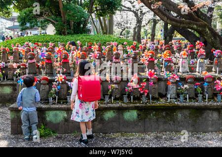 Zwei Schüler vor Jizo Statuen mit roten Kappen, schützenden Gottheiten für verstorbene Kinder, Ungeborene Kinder Garten. Zojoji Tempel Stockfoto