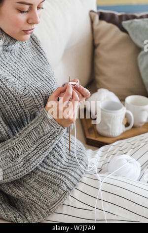 Mädchen in einem warmen Grau Pullover strickt Sitzen auf einem Sofa in einem gemütlichen Interieur hygge Stockfoto