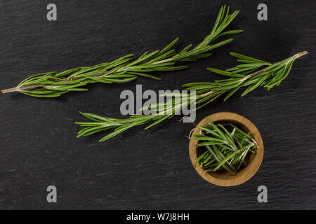 Gruppe von zwei ganze Menge Stücke von frischem immergrüne Zweig Rosmarin in eine hölzerne Schüssel flatlay am grauen Stein Stockfoto