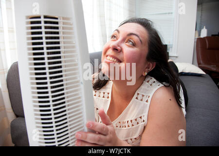 A woman who is warm in the heat hugs and looks up lovingly at her air fan Stockfoto
