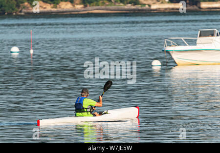 Ein Mann ist Kajakfahren in einem Hafen an der Nordküste von Long Island paddeln um verankerten Boote. Stockfoto