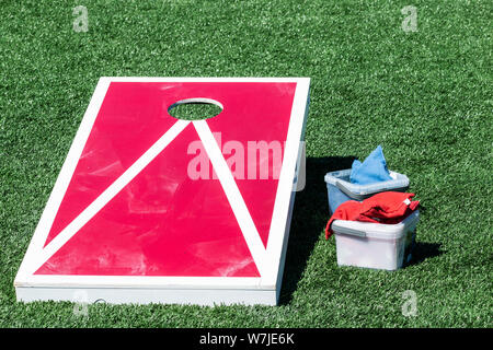 Red mais Loch Spiel mit weißen Streifen auf grünem Rasen Feld mit blauen und roten Bohne Beutel in Containern Nest. Stockfoto