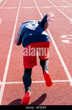 Ein High School sprinter ist das Üben der Beginn des Rennens im Winter auf einen Track. Bild aus hinter den Athleten genommen. Stockfoto