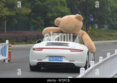 Ein chinesischer Mann der 'Reichen'-Laufwerken der zweiten Generation einen Porsche Luxus Auto mit einem 2,5 Meter hohen Riesen Puppe Bär oben gefüllte der Beifahrersitz in Hangzhou Stockfoto