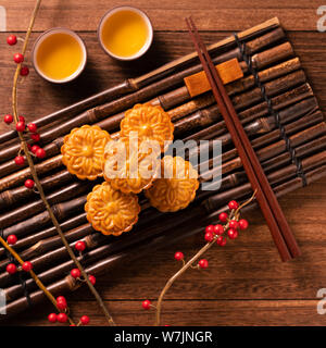 Traditionelle chinesische Gebäck Moon Cake Mooncake mit Tee Tassen auf Bambus Serviertablett auf hölzernen Hintergrund für Mondfest, Ansicht von oben, flach. Stockfoto