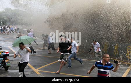 Besucher und Anwohner laufen weg wie Wellen aus einem Tidal Bore Schwankung hinter einer Barriere am Ufer des Qiantang Fluss in Hangzhou City, East China Zh Stockfoto
