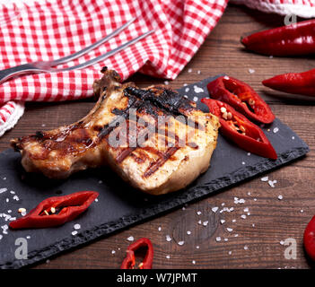 Stück gebratenes Schweinefilet auf ein Knochen liegt auf einem schwarzen Brett, saftiges Fleisch, Nahaufnahme Stockfoto