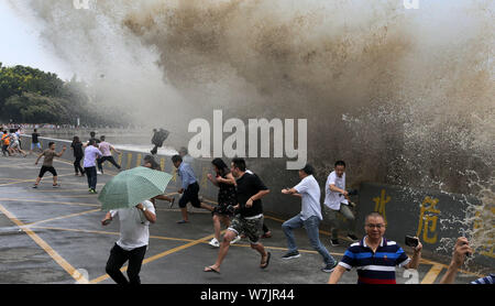 Besucher und Anwohner laufen weg wie Wellen aus einem Tidal Bore Schwankung hinter einer Barriere am Ufer des Qiantang Fluss in Hangzhou City, East China Zh Stockfoto
