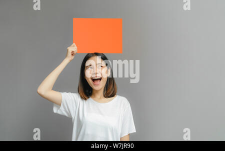 Asiatische Frau glücklich lächelnde Holding eine leere orange Poster auf grauem Hintergrund. mit leeren Platz für Text. Stockfoto