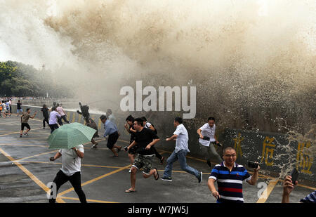 Besucher und Anwohner laufen weg wie Wellen aus einem Tidal Bore Schwankung hinter einer Barriere am Ufer des Qiantang Fluss in Hangzhou City, East China Zh Stockfoto