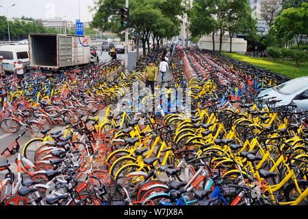---- Fußgänger Spaziergang durch Fahrräder von mobike (orange), ofo (Gelb) und anderen Chinesischen bike Dienstleistungen entlang einer Straße in Peking geparkt, C Stockfoto