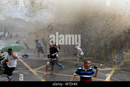 Besucher und Anwohner laufen weg wie Wellen aus einem Tidal Bore Schwankung hinter einer Barriere am Ufer des Qiantang Fluss in Hangzhou City, East China Zh Stockfoto