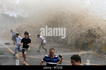 Besucher und Anwohner laufen weg wie Wellen aus einem Tidal Bore Schwankung hinter einer Barriere am Ufer des Qiantang Fluss in Hangzhou City, East China Zh Stockfoto