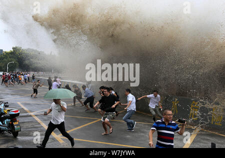 Besucher und Anwohner laufen weg wie Wellen aus einem Tidal Bore Schwankung hinter einer Barriere am Ufer des Qiantang Fluss in Hangzhou City, East China Zh Stockfoto