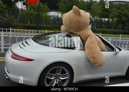 Ein chinesischer Mann der 'Reichen'-Laufwerken der zweiten Generation einen Porsche Luxus Auto mit einem 2,5 Meter hohen Riesen Puppe Bär oben gefüllte der Beifahrersitz in Hangzhou Stockfoto