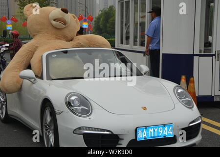 Ein chinesischer Mann der 'Reichen'-Laufwerken der zweiten Generation einen Porsche Luxus Auto mit einem 2,5 Meter hohen Riesen Puppe Bär oben gefüllte der Beifahrersitz in Hangzhou Stockfoto