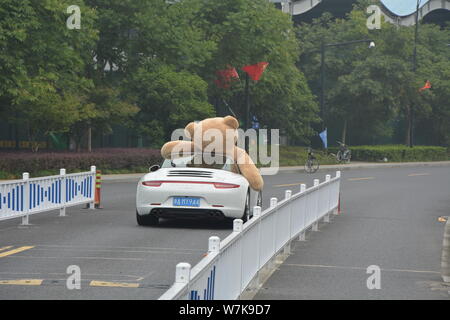 Ein chinesischer Mann der 'Reichen'-Laufwerken der zweiten Generation einen Porsche Luxus Auto mit einem 2,5 Meter hohen Riesen Puppe Bär oben gefüllte der Beifahrersitz in Hangzhou Stockfoto