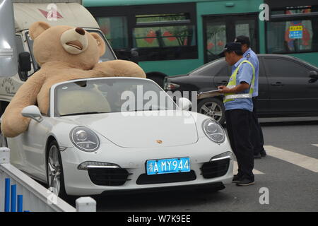 Ein chinesischer Mann der 'Reichen'-Laufwerken der zweiten Generation einen Porsche Luxus Auto mit einem 2,5 Meter hohen Riesen Puppe Bär oben gefüllte der Beifahrersitz in Hangzhou Stockfoto