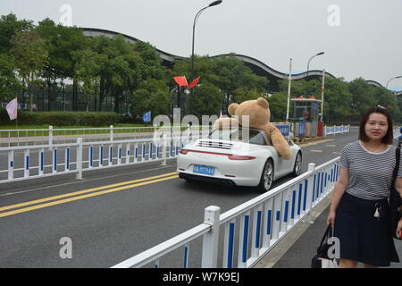 Ein chinesischer Mann der 'Reichen'-Laufwerken der zweiten Generation einen Porsche Luxus Auto mit einem 2,5 Meter hohen Riesen Puppe Bär oben gefüllte der Beifahrersitz in Hangzhou Stockfoto