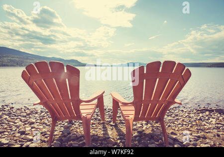 Zwei Stühle aus Holz am Ufer eines Sees mit Blick auf das Wasser. Stockfoto