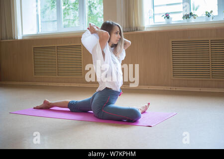 Junge akrobatische Frau mit blonden Haaren sitzen auf der Yogamatte und Dehnübungen Stockfoto