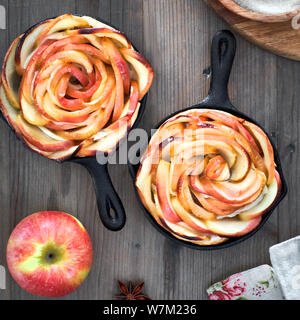 Hausgemachte Blätterteig mit Rose geformte Apfelspalten gebacken in Eisen skillets. Top lag auf Holzbrett mit Apple und Zucker. Flach, quadratische Komposition. Stockfoto