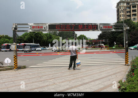 Ein Fußgänger wartet auf ein rotes Licht vor der geschlossenen automatische Seil System auf einer Straßenkreuzung in Wuhan City grün, der Central China Hube Stockfoto