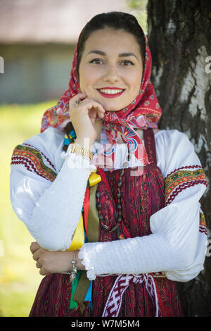 Junge Frau in der traditionellen russischen Kleidung stand unter einem Baum und hält Hand am Gesicht - mit Blick zur Kamera Stockfoto