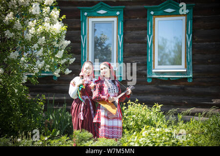 Zwei junge Frauen in der traditionellen russischen Kleidung stehen vor einem Holzhaus ein Thema spielen Balalaika Stockfoto