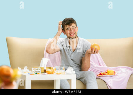 Junge Menschen leiden unter Allergie gegen Zitrusfrüchte. In Hautausschlag, Jucken, Niesen in die Serviette, sitzt von grapefruits und Orangen umgeben. Einnahme von Medikamenten ohne Ergebnis. Healthcare Konzept. Stockfoto