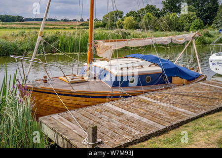 Eine traditionelle hölzerne Segelboot gebunden bis zu einer hölzernen Kai Position auf dem Fluss Bure auf der Norfolk Broads Stockfoto