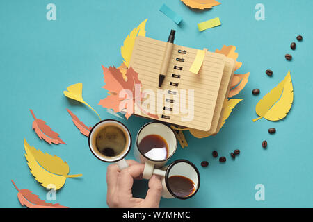 Herbst Planung, kreative, oben flach auf mint Farbe Papier Hintergrund legen. Hand mit drei Tassen Kaffee und offenen leer Notebook mit Herbst leav Stockfoto