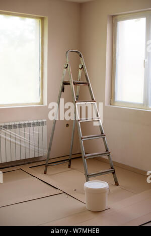 Malerei die Wände im Zimmer mit Walze und Leiter während der Sanierung. Die Fenster sind mit Nylon verpackt. Bild Stockfoto