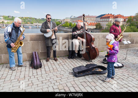 Prag, Tschechische Republik - 30. April 2017: Band der Straßenmusikanten spielt für Touristen auf der Karlsbrücke in Prag. Kleines Mädchen setzt Geld in einer Git Stockfoto