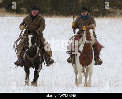 Zwei Cowboys reiten im Schnee, mit Gewehren, Wyoming, USA, Februar 2012, Modell freigegeben Stockfoto