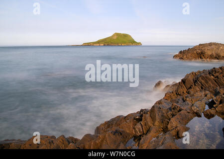 Lange Belichtung von Kalksteinfelsen, die von Wellen mit dem Kopf der Wurm im Hintergrund gewaschen, abgeschnitten vom Festland auf eine Insel bei Flut, Rhossili, die Halbinsel Gower, Wales, Großbritannien, Juli. Sequenz 3 von 3 Passende Ansichten zu verschiedenen Gezeiten Stockfoto