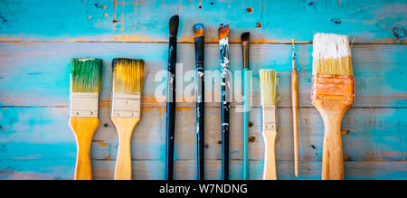 Satz von Pinsel für Künstler und Dekorateur auf einem blauen Holztisch - Begriff der Kunst und der Arbeit zu Hause - oben - schmutzige Farben für einen schönen Stockfoto