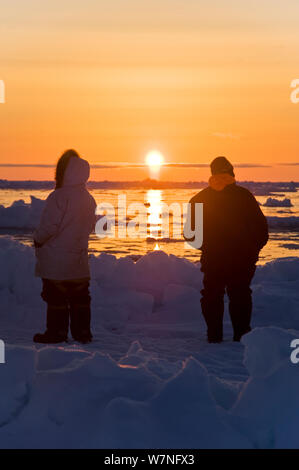 Silhouette der Inupiaq Aufenthaltskosten walfänger am Rande einer Leitungsunterbrechung im Packeis, suchen die bowhead Wale Mitte der Sonne folgt den Horizont. Chukchi Sea, offshore von Barrow, arktischen Küste von Alaska, Mai 2012. Stockfoto