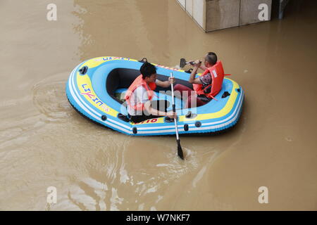 Die anwohner nehmen ein aufblasbares Schlauchboot auf einer überfluteten Straße durch starken Regen in Liuzhou City, South China Guangxi Zhuang autonomen Region verursacht, Stockfoto