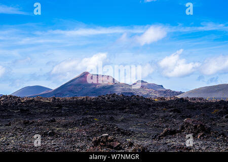 Spanien, Lanzarote, Roten Riesen Vulkan hinter endlosen schwarzen ariden Lavafeld Stockfoto