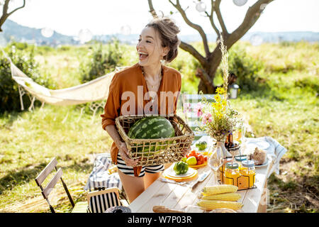 Junge Frau, dekorieren und servieren Tisch, Wassermelone während der Vorbereitung für die festlichen Mittagessen im wunderschönen Garten bei schönem Wetter Stockfoto