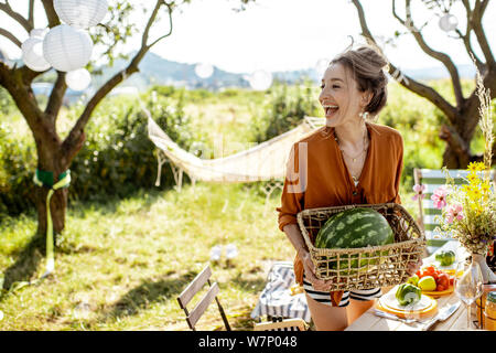 Junge Frau, dekorieren und servieren Tisch, Wassermelone während der Vorbereitung für die festlichen Mittagessen im wunderschönen Garten bei schönem Wetter Stockfoto