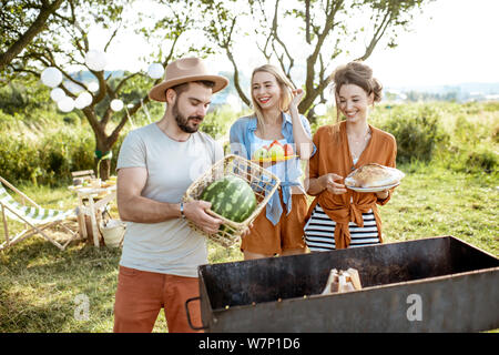 Junge Freunde Spaß während der Vorbereitung für die Abendessen, zusammen mit Nahrungsmitteln in der Nähe des Grill im Garten Stockfoto