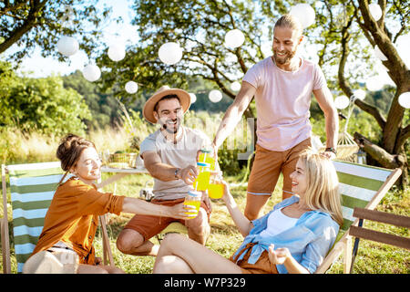 Junge und fröhliche Freunde entspannt auf den Sonnenliegen, klirren Gläser in die wunderschön gestalteten Hinterhof oder im Garten während einer feierlichen Sitzung Stockfoto