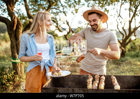 Paar Freunde mit Grill, kochen Essen im wunderschönen Garten bei einem festlichen Mittagessen auf einem Sommer aftenoon Stockfoto