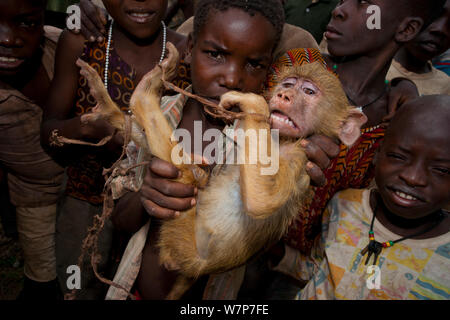 Kinder in Mosambik mit traumatisierten gefangenen Yellow baboon (Papio cynocephalus) Junge, gefangen bei der Truppe Erntegut überfallen. Pemba, Montepuez Highway, nord-östlichen Mosambik. Stockfoto