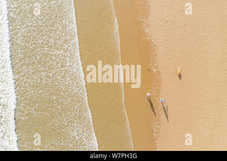 Luftaufnahme von Menschen zu Fuß und ihre Schatten auf einen Sandstrand, neben der Wellen in Porthcawl Wales UK Stockfoto