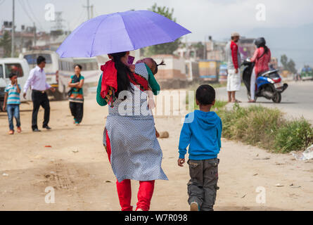 Mutter und Kind mit Regenschirm ihr Baby an der Seite einer städtischen Straße in Kathmandu. Stockfoto