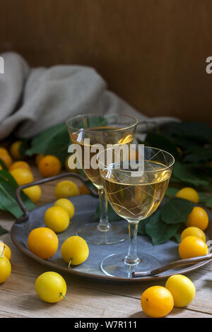 Cherry Plum Likör in kleinen Gläsern und Cherry Plum auf einer hölzernen Hintergrund. Im rustikalen Stil. Stockfoto